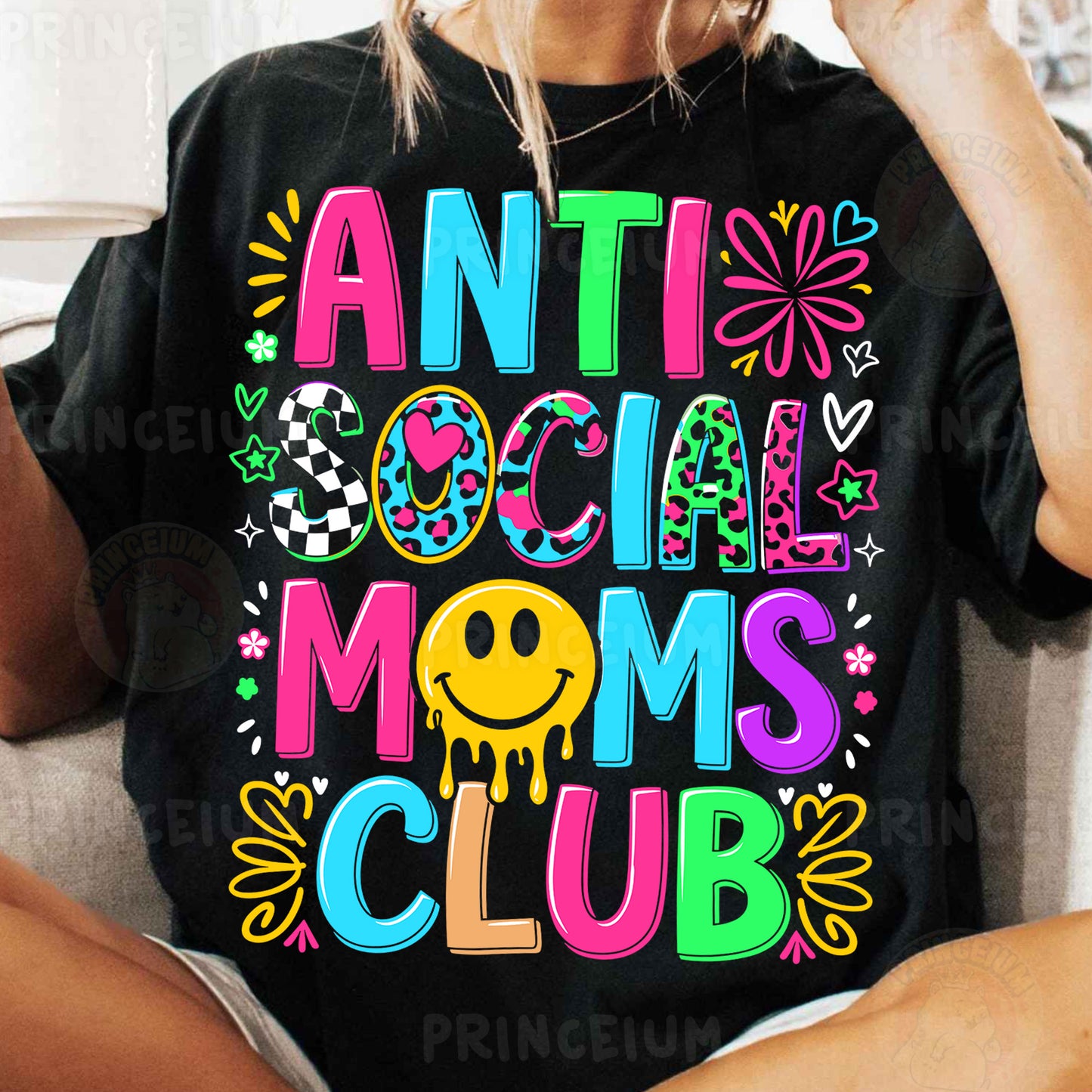 a woman sitting on a couch wearing an anti social moms club shirt