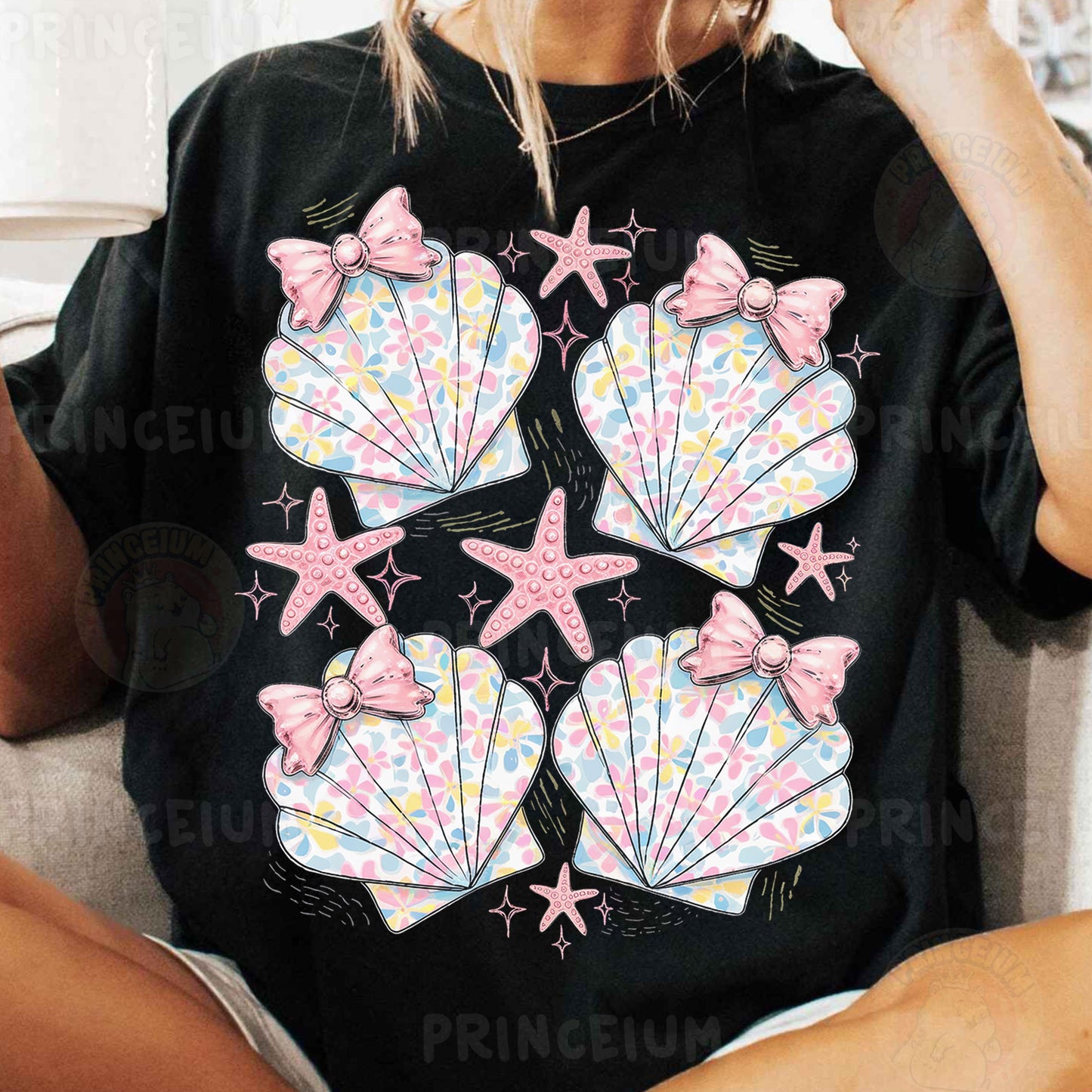 a woman sitting on a couch wearing a black shirt with pink bows and seashell