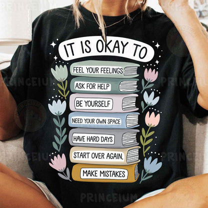 a woman sitting on a couch wearing a t - shirt that says it is okay